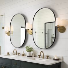 two round mirrors are hanging above the double sink vanity in this bathroom with white walls and gold fixtures