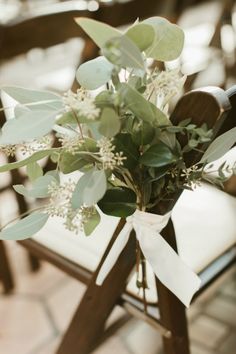 an arrangement of flowers and greenery tied to a wooden chair at a wedding ceremony