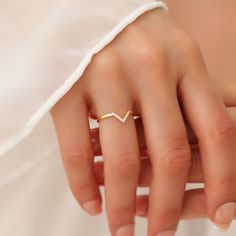 a woman's hand wearing a gold chevron ring on her left finger, with a diamond in the middle