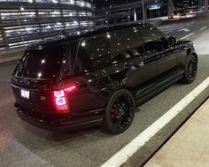 a black range rover is parked on the side of the road at night with its lights on