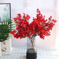 red flowers are in a glass vase next to a potted plant on a table