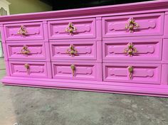 a large pink dresser with gold handles and knobs on the doors is sitting in a garage