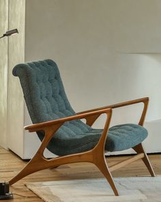 a blue chair sitting on top of a wooden floor next to a white rug and lamp