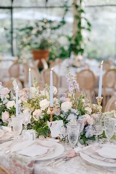 the table is set with white and pink flowers, silverware, candles, and napkins