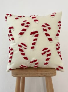 a white pillow with red and white candy canes on it sitting on a wooden stool