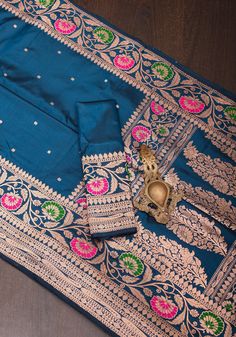 This breathtaking Prussian Blue  saree showcases a contemporary interpretation of Banaras' classic weaving techniques. Adorned with intricate chunri zari buttas throughout the body, it is accompanied by a vibrant meenakari Zari floral border and pallu, infusing the luxurious silk fabric with a pop of color. If you admire a unique blend of design, texture, and shades, this saree will captivate your senses. SILK MARK CERTIFIED This saree is ready to wear with fall and pico done. Handmade silk tassels adorn the pallu and add more grace to it. An unstitched blouse fabric is included. *Note: There may be minor variations in the shade, the texture of the product. Hues/textures show differently due to variations in screen settings and other factors, *Note: This saree is woven of pure natural silk Luxury Women's Sets With Zari Weaving, Luxury Banarasi Silk Sets With Meenakari, Luxury Designer Sets With Zari Weaving, Luxury Blue Suits For Fall, Luxury Silk Fabric With Zari Weaving, Banarasi Katan Silk Saree, Silk Tassels, Design Texture, Katan Silk Saree