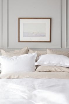 a bed with white linens and pillows in a room that is painted pale grey