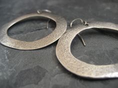 This item is made to order please allow 5 to 8 business days for your order to ship. A simple earring, yet with a lot of character. This is a great alternative to the classic round hoop. These whimsical hoop earrings where hand carved and cast .925 sterling silver. They have been lightly oxidized to reveal the uneven texture, which gives these earrings an organic feel. They measure 1 1/2 inches in width and 1 1/4 inches in height, and hang of a sterling silver ear wire. Silver Oval Earrings For Everyday, Hand Forged Silver Circle Jewelry, Hand Forged Silver Circular Jewelry, Unique Sterling Silver Hoop Earrings For Pierced Ears, Minimalist Silver Earrings With Sterling Silver Clasp, Silver Small Hoop Earrings Stamped 925, Oxidized Finish Hoop Earrings As Gift, Unique Silver Nickel-free Hoop Earrings, Oxidized Round Hoop Earrings As Gift