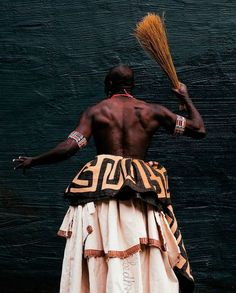 a man in an african dress holding a broom and looking at the wall behind him