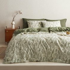 a bed with green comforters and pillows in a room next to a dresser, lamp and vase