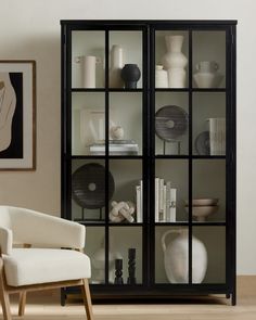 a white chair sitting in front of a black book shelf filled with books and vases