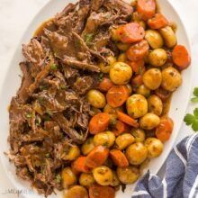 a white plate topped with meat, potatoes and carrots next to a blue napkin