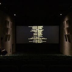 an empty theater with rows of seats in front of a screen that has words projected on it