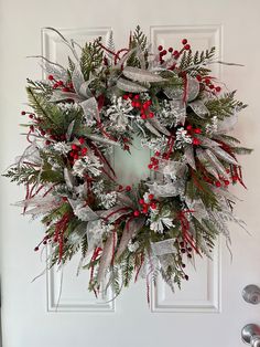 a christmas wreath hanging on the front door with red berries and silver ribbon around it