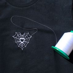 a spool of thread next to a t - shirt with a spider web on it