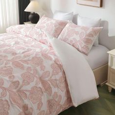 a bed with pink and white comforters in a bedroom next to a night stand