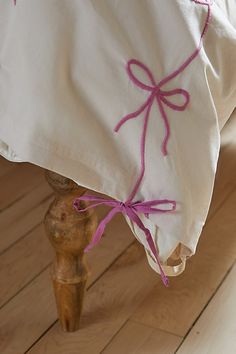 a white pillow with pink ribbon tied to it on a wooden stool in front of a window