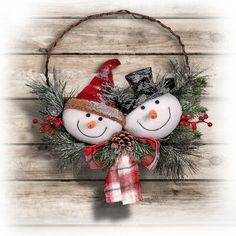 two snowmen with hats and scarfs are hanging on a wooden wall in front of a wreath