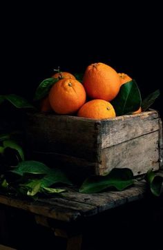 a wooden crate filled with oranges sitting on top of green leaves next to a black background