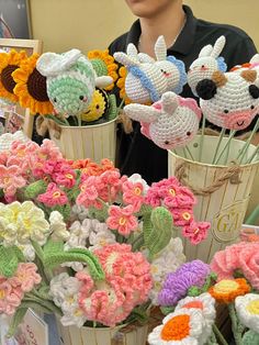 there are many crocheted flowers in vases on the table and one person is looking at them