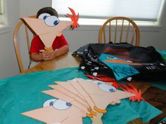 a young boy sitting at a table with paper cut out of cartoon characters on it