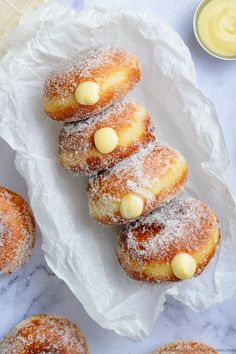 powdered sugar covered doughnuts are arranged on a white paper with butter in the background