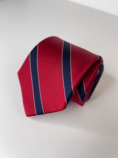 a red and blue striped tie laying on top of a white table next to a pen