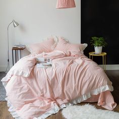 a bed with pink sheets and pillows in a room next to a white rug on the floor