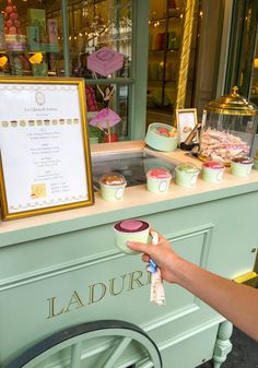 a person is holding a cupcake in front of a display case with various desserts on it