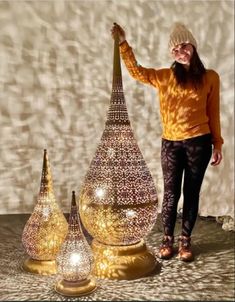 a woman is standing next to three large vases with lights on them and one has her arm in the air