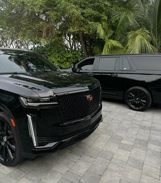 two black suvs parked next to each other in front of some trees and bushes