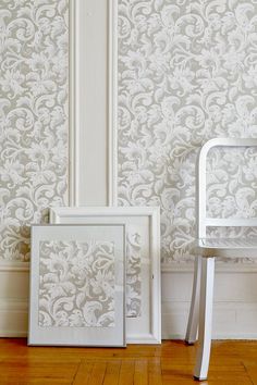 two white chairs sitting next to each other in front of a wallpapered room