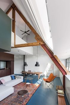 a living room filled with furniture next to a loft style ceiling fan and window covered in wood beams