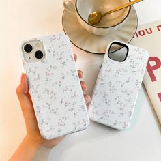 two white iphone cases sitting on top of a table next to a cup and saucer