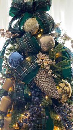 a christmas tree is decorated with green and gold ribbons, pine cones, ornaments and bows