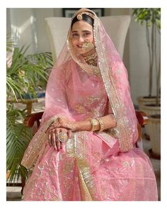 a woman wearing a pink and gold bridal gown sitting in a chair with her hands on her hips