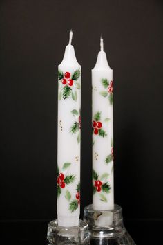 two white candles with holly and red berries on them are sitting next to each other