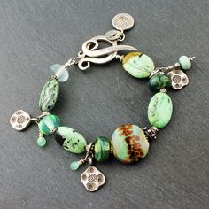 "Beautiful green turquoise oval gemstones are combined with sterling silver, and my lampwork glass beads in this handmade bracelet. Sweet sterling silver charms dangle from the bracelet, as well as my tiny fine silver and glass beads. A decorative sterling silver toggle clasp and a dangle of a lotus flower silver charm complete the design. So perfect for Spring and Summer! This lovely new bracelet will fit an 7\" wrist and can be re-sized at no extra charge. Your bracelet will arrive artfully pa Green Sterling Silver Bracelets With Silver Beads, Green Sterling Silver Bracelet With Silver Beads, Handmade Green Beaded Bracelets With Oval Beads, Handmade Green Bracelets With Oval Beads, Spiritual Green Beaded Sterling Silver Bracelets, Green Sterling Silver Beaded Bracelet, Green Beaded Sterling Silver Bracelet, Green Sterling Silver Bracelets With Round Beads, Unique Green Sterling Silver Bracelets