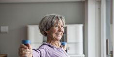 an older woman holding two blue dumbs in her right hand and smiling at the camera