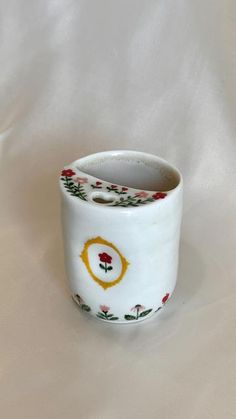 a white vase with red and yellow flowers on it's sides, sitting on a white surface