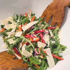 a salad in a white bowl with wooden spoons on the side next to it