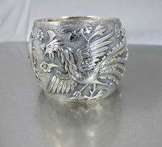 Fabulous beautifully detailed antique Qing Dynasty Chinese wide Sterling Silver bangle Bracelet with raised image of a Phoenix and a Dragon with what looks like the Sun at the center.  According to the hallmark CHINA 100 23 this piece is mid19th century and may have been one of a pair of Wedding Bracelets.  The Dragon represents the Masculine with its strength and power, while the Phoenix embodies the feminine, representing grace and beauty.  Together they signify the harmonious union of opposites. A stunning piece that will become a family heirloom for many years to come. A wonderful addition to your antique jewelry collection! Bracelet is in great condition. Opens and closes securely.  Hallmarked CHINA 100 23. Measures 2.25 inches from top to bottom and the inside measures 6.50 inches ar Victorian Etched Cuff Bracelet For Wedding, Antique Round Cuff Bracelet For Wedding, Antique Etched Bangle For Wedding, Antique Hallmarked Cuff Bracelet For Wedding, Antique Etched Wedding Bangle, Victorian Style Ceremonial Cuff Bracelet With Intricate Design, Victorian Cuff Bracelet With Intricate Design For Ceremonial Occasions, Victorian Cuff Bracelet With Intricate Design For Ceremonial, Ornate Engraved Bangle For Wedding