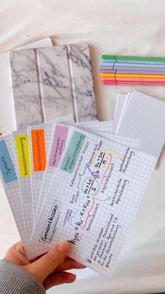 a person holding five notebooks in their hand with colored paper on the top and bottom