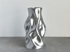 a silver vase sitting on top of a cement floor next to a wall with white walls in the background