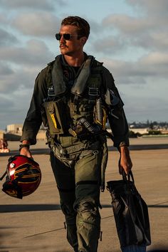 a man walking across an airport holding a helmet on his shoulder and carrying a bag