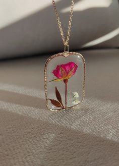 a pink rose in a glass vase on a gold chain