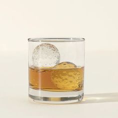 a glass filled with liquid and an ice ball sitting on top of a white table