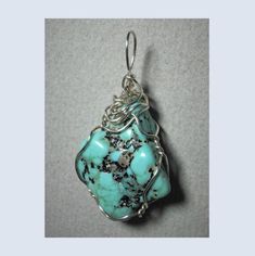 "Turquoise Nugget Pendant Wire Wrapped in .925 Sterling Silver Round Wire This inspiring stone offers a few small pebbles of golden pyrite nestled inside a light to medium turquoise-blue and black patterned background. Best worn with blue, green, coral, orange, or red; but quite versatile, and many dark, bright, pastel, and earth tone colors also wear well, especially black, grays, brown, beige/tan, and lavender. A similar color of turquoise will blend, so should be avoided. Some darker purple colors tend to clash. Take caution with yellows as well. Description: A light to bright turquoise-blue with black oxidation and very small pebbles of golden pyrite; rounded kite shaped, and opaque stone, wrapped in 22 gauge sterling silver wire. Stone Size: Medium (1-1/16\" x 7/8\" x 7/16\"). Pattern Artisan Turquoise Necklace With Large Stone, Artisan Blue Turquoise Necklace Untreated, Turquoise Wire Wrapped Pendant Necklace, Untreated Chrysocolla Turquoise Jewelry, Handmade Turquoise Chrysocolla Necklace, Artisan Turquoise Jewelry For Healing, Unique Turquoise Chrysoprase Jewelry, Healing Howlite Turquoise Jewelry, Healing Turquoise Howlite Jewelry