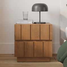 a nightstand with a lamp on top of it next to a green bed sheet and pillows