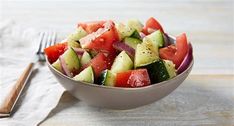 a bowl filled with cucumbers and tomatoes next to a fork on top of a table